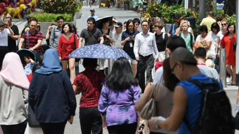 Getty Images Pedestrians wait to cross the street along the Orchard Road shopping district in Singapore on February 21, 2018.