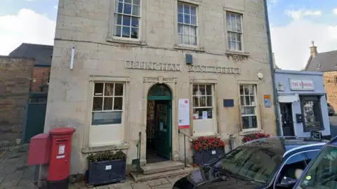 A view of a cream-coloured brick building which serves as Uppingham Post Office. A red post box is visible out front.