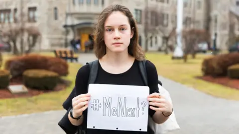 Deborah Lowery Violet Massie holding up a sign reading 'Me Next?'