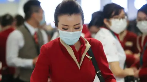 Getty Images A flight crew from Cathay Pacific Airways, wearing protective masks, gather in the international terminal after arriving on a flight from Hong Kong.