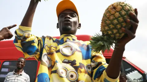 A fruit seller in a Minions shirt holds up pineapples in Abuja, Nigeria - Thursday 9 April 2020