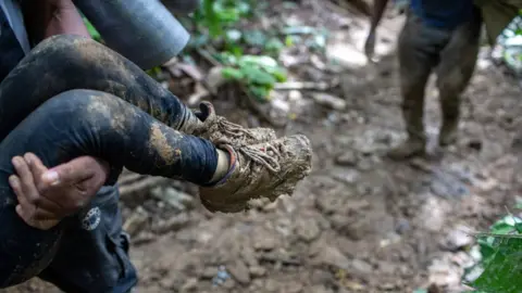 Getty Images A Colombian guide carries a Haitian child up a mountain slope near Colombia's border with Panama on October 19, 2021 in the Darien Gap, Colombia.