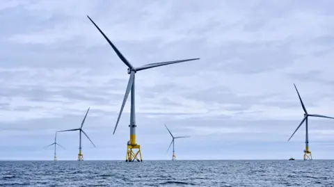 A set of offshore wind turbines out at sea with greyish blue skies in the background