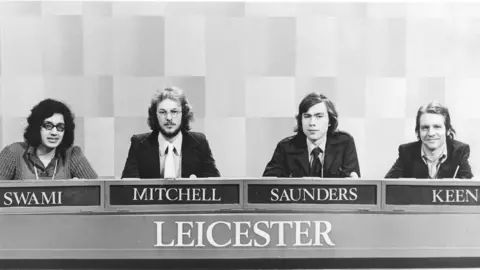 A black and white picture of a team from the 1970s, in formation with their names underneath, with three white men joined by one South Asian woman