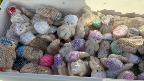 A close-up view inside a white wooden box filled with many small teddy bears.