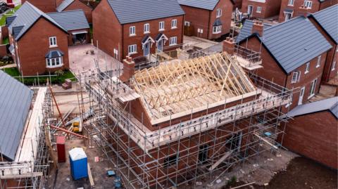 A new-build housing estate with some completed homes, others still under construction surrounded by scaffolding.
