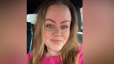 Lydia Little Lydia smiles at the camera. She has long hair and a pink jumper on. She is sitting in a car.