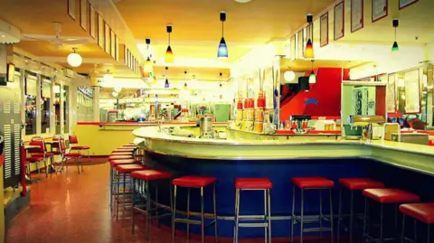 The Harbour Bar, Scarborough Red stools line the G-shaped bar of an ice cream parlour. The room is red and yellow, in the style of a 1950s American diner.