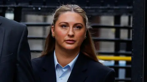 Reuters Ms Hand with long blonde hair, she is wearing a blue shirt and navy blazer as she leaves court.