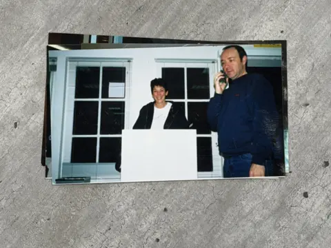 Chauntae Davies A woman, Ghislane Maxwell, with a short haircut smiles and stands behind a white podium to her left a man, Kevin Spacey, has a cell phone on his right ear. He is wearing a navy shirt and blue jeans.