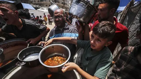 Palestinians wait in line to receive hot meals distributed by charity organizations while Israel's destructive attacks continue on 7 June, 2025.