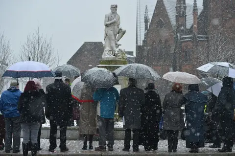 Getty Images A statue of Robert Burns in Dumfries on a snowy day with lots of people with umbrellas
