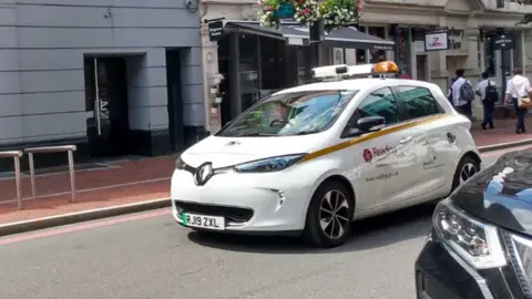 A Renault electric car with Reading Borough Council branding on the front car door in Reading town centre.