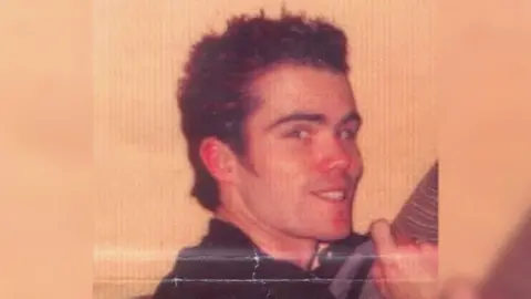 PSNI Martin Kelly smiling at the camera, he has dark hair and dark clothing on.