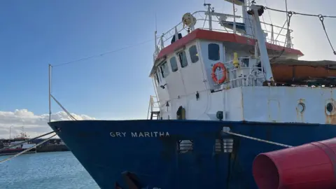 BBC The bow of a large blue cargo vessel. She is moored to a quay in Penzance dock.