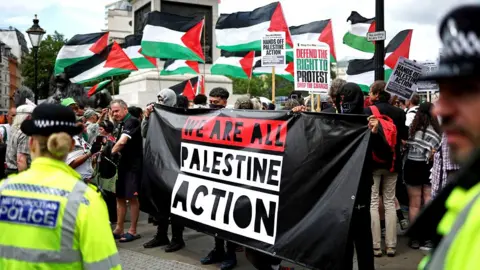 Police officers monitor protesters holding a banner during a protest in support of pro-Palestinian group Palestine Action, in Trafalgar Square, central London, on June 23, 2025