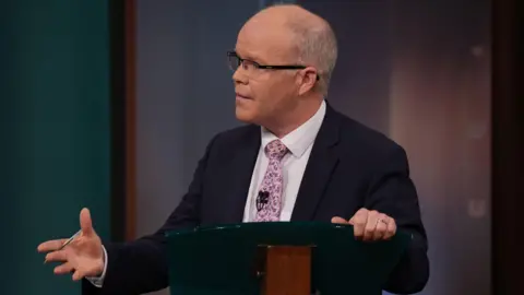 PA Media A man with grey hair, glasses and wearing a dark suit with pink tie