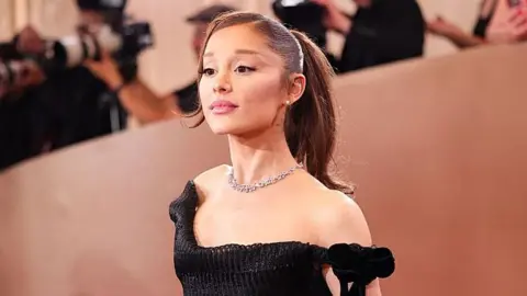 A brunette woman in a black off-the-shoulder dress poses for the camera.