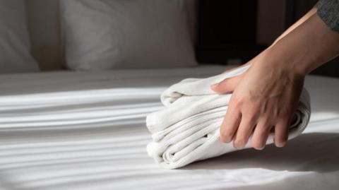 Close up of hotel worker's hands arranging the stack of towels on bed in hotel bedroom