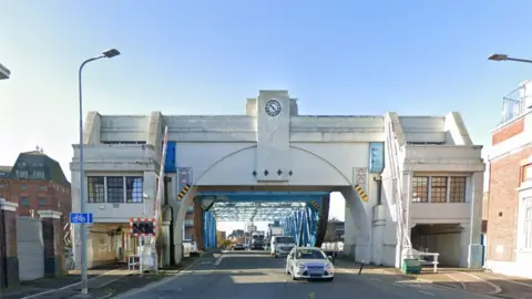 North Bridge across the River Hull with cars driving across. It has a white concrete archway with covered walkways and a blue bridge structure behind.