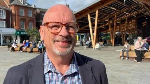 Andrew Turner/BBC Jonathan Newman is standing near Great Yarmouth Market Place. He is smiling and is wearing a blue jacket.