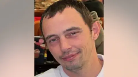 A man with short brown hair smiles at the camera