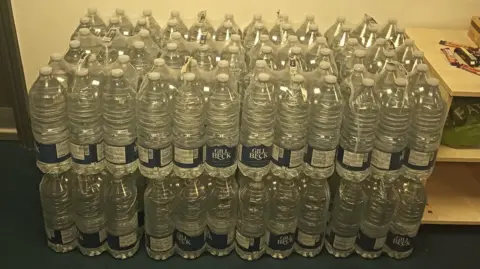 David Flanighan Dozens of two-litre bottles of water stacked on top of each other
