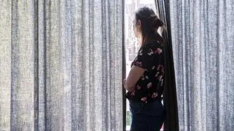 A woman wearing black trousers' and a top looking out of a window