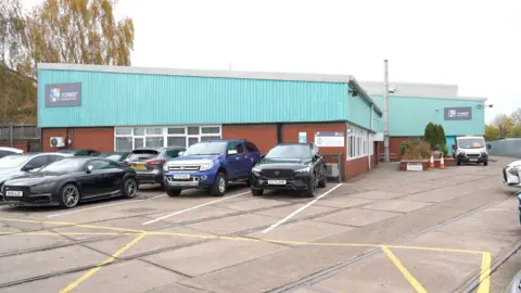 The Tecforce building is partly blue and the rest made up of brick. Several cars are parked in front.