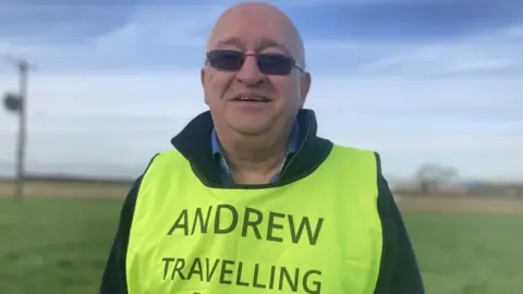 Jessica Lane/BBC Andrew Elliker-Reeve wearing dark glasses and a yellow-coloured vest with the words "Andrew Travelling Blind" written on the front