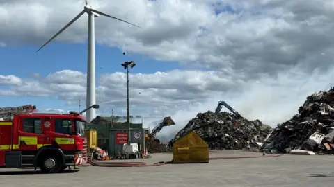 A fire engine site at a landfill site, with smouldering rubbish.