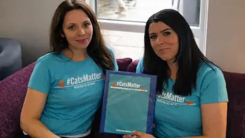 Mandy Hobbis Tiya Ivy (left) and Mandy Hobbis (right) both wear T-shirts with '#CatsMatter' printed across it. Between them, they are holding a document with the same branding. 