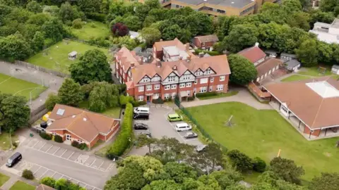 An aerial view of Bradstow school. it is a large manor-type, red brick building surround by trees and green fields