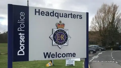 BBC Sign outside Dorset Police HQ bearing the force's badge. The blue and white sign reads: Dorset Police Headquarters Welcome