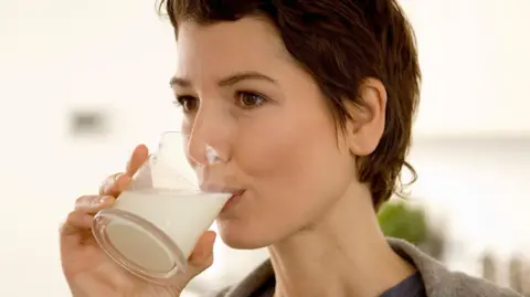 Getty Images A woman with short brown hair drinks milk from a glass held to her lips