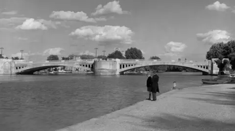 Getty Images A black and white picture of Caversham Bridge and the River Thames, with two boys stood on the edge of the river. 