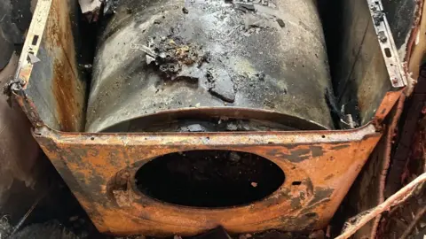 A burnt out tumble driver sitting in an alcove with charred walls