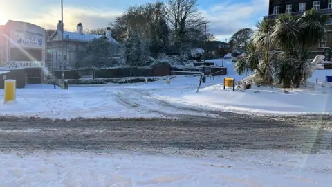 A roundabout covered in snow, with dirty tracks where vehicles have driven through.