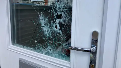 A pane of glass on a front door with a number of bullet holes 