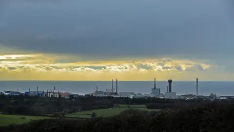 A general view of the skyline of the Sellafield site, pictured in between grassy fields and the sea.