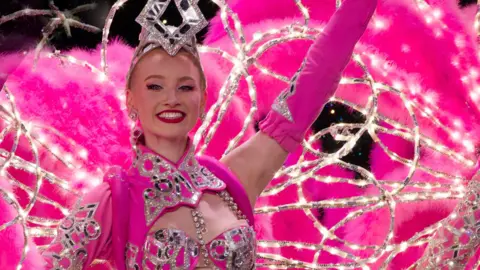 Handout Amelia dressed in a pink cabaret costume on stage