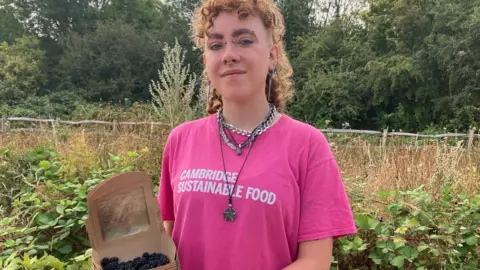 Alex Vardill wearing a pink T-shirt, smiling straight at the camera and holding a box of blackberries.