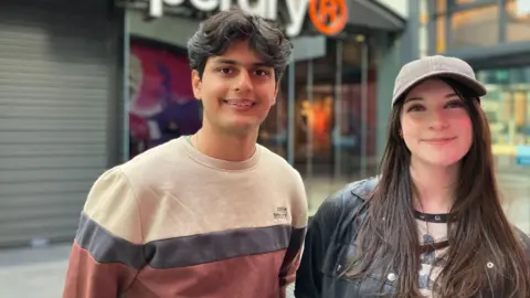 Arthav Naphde and Elena Harris stand inside a shopping centre, smiling at the camera