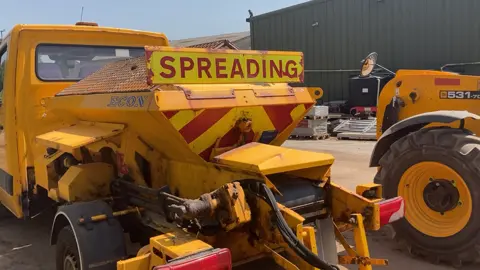 A yellow gritting lorry outside a depot
