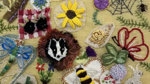 ArtHouse Jersey A close-up of some of the embroidery, which includes a black and white badger on a brown background, a yellow sunflower and a black and yellow bee with white wings and brown-ish stitching around it.