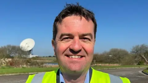 A picture of Matthew Cosby - he is wearing a blue suit shirt, black blazer and hi-visibility jacket.