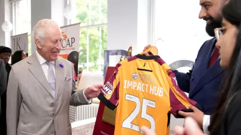 PA Media King Charles holding a Bradford City AFC top with Impact Hub 25 on the back