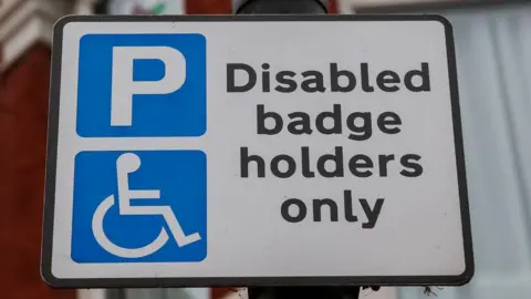 Getty Images A street sign attached to a lamppost which says, Disabled badge holders only, on it in black writing.