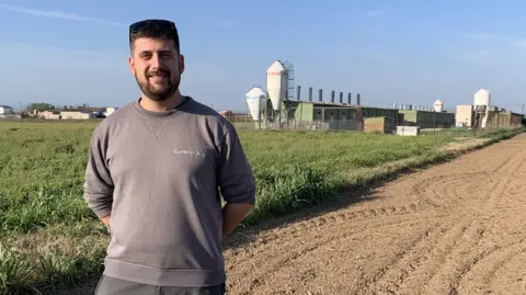 Pig farmer Jordi Saltiveri stands on his farm, with a field and buildings in the background