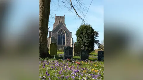 Richard Chatham A view of St Mary's Church. Grave stones sit in the church yard outside the church and wild flowers in a variety of colours grow around the yard.